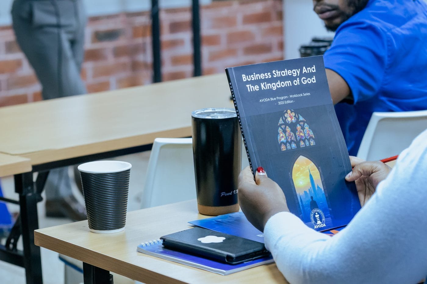 An AVODA Blue founder holding the Business Strategy and the Kingdom of God workbook during class